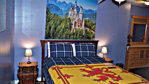 Un dormitorio con cama, dos lámparas de noche, una mesita de noche de madera, un aparador y un cartel grande con temática de castillo en la pared.