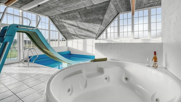 Piscina interior moderna com escorrega, banheira de hidromassagem e grandes janelas que proporcionam luz natural.