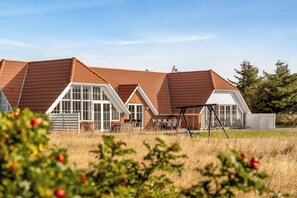 A large house with a sloped roof, multiple windows, and a patio area with outdoor furniture. - Family-friendly holiday home with pool, located close to the North Sea in Vrist. (Harboøre)