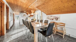 Uma sala de jantar ampla com uma longa mesa de madeira, cadeiras pretas e iluminação pendente.