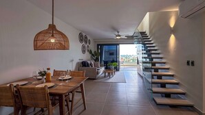 Un comedor moderno con una mesa y sillas de madera, una lámpara colgante y una escalera que conduce a un área exterior.