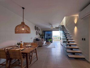 Un comedor moderno con una mesa y sillas de madera, una lámpara colgante y una escalera que conduce a un área exterior.