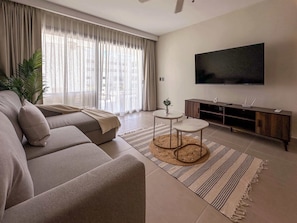 A modern living room with a sofa, a TV, a small table, and a plant.