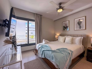 A hotel room with a bed, a desk, a ceiling fan, and a window with curtains.