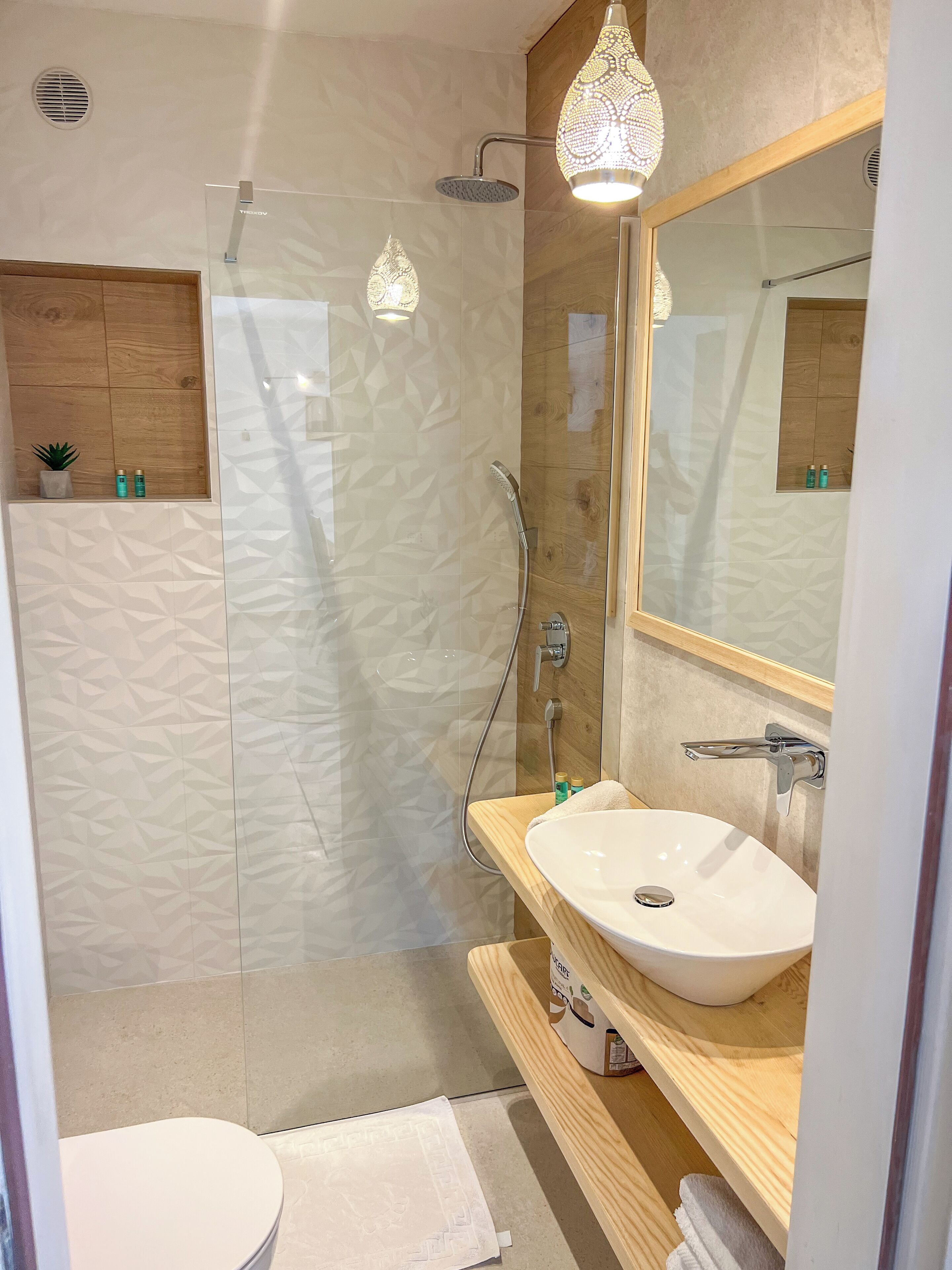 Un baño moderno con cabina de ducha de vidrio, tocador de madera con lavamanos blanco y un espejo grande.