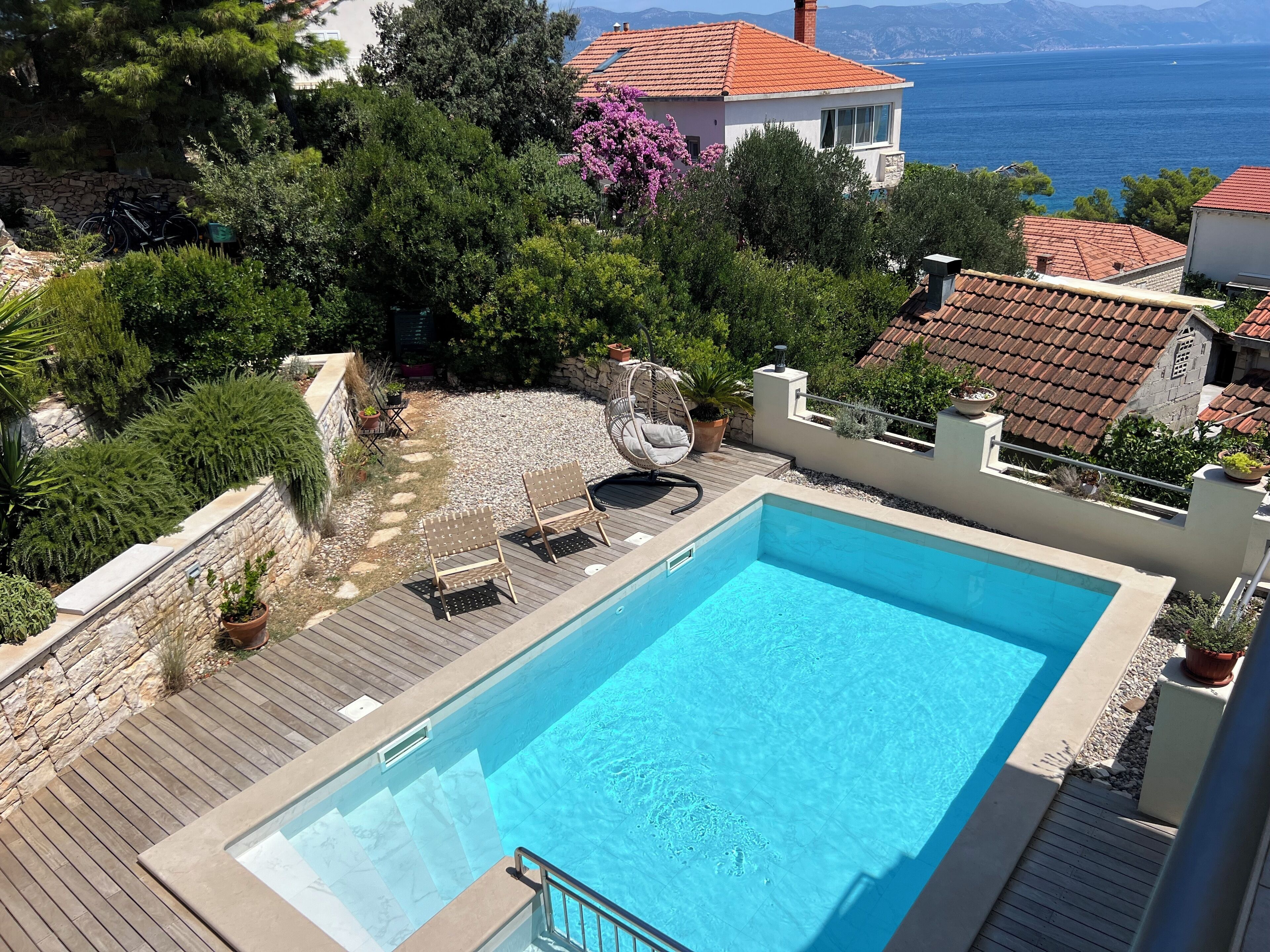 Une piscine dotée d’une terrasse en bois, entourée de murs en pierre et agrémentée de plantes en pot.