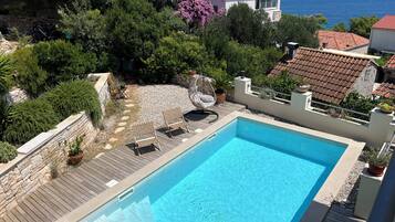 Une piscine dotée d’une terrasse en bois, entourée de murs en pierre et agrémentée de plantes en pot.