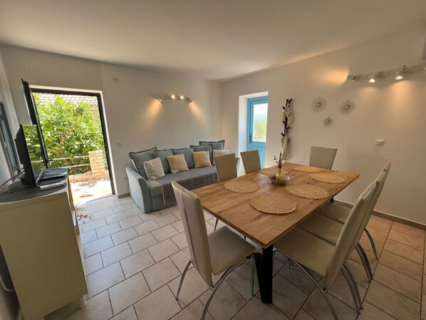Un comedor con mesa de madera, sillas color beige y sofá gris.