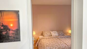 A bedroom with a bed, two bedside lamps, a pillow with a quote, and a framed picture on the wall.