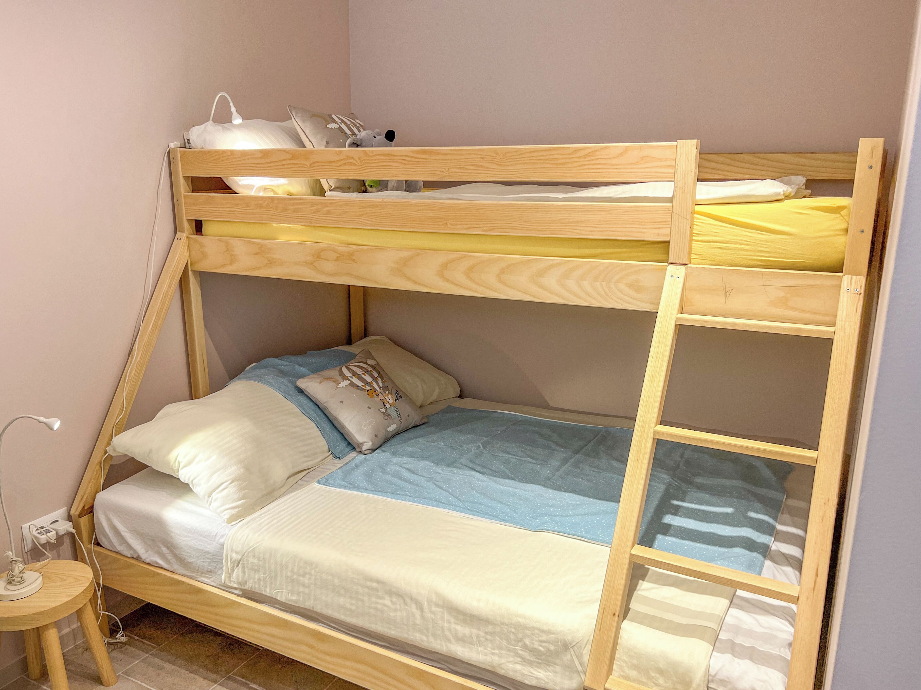 Una cama individual superpuesta con escritorio, silla, lámpara y enchufe.