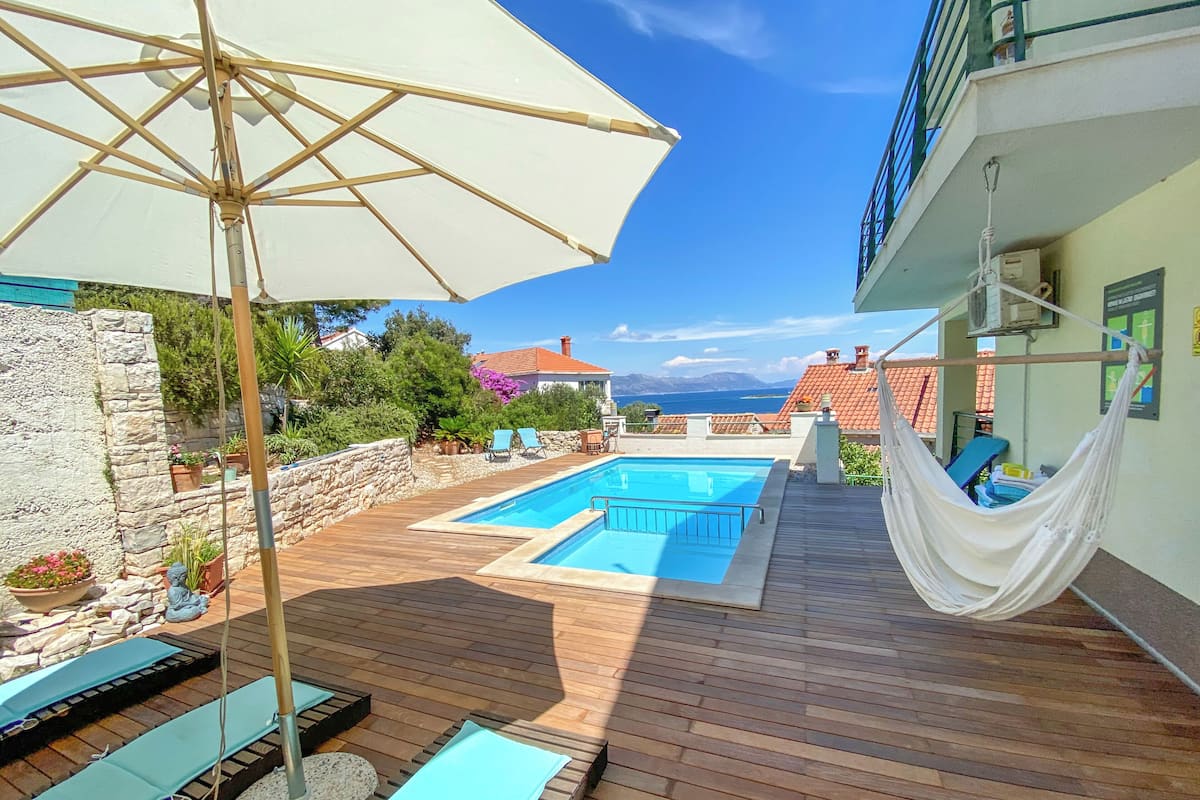 Una terraza de madera con piscina, sillas de descanso y una hamaca.