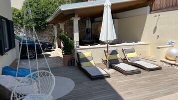 A poolside area with lounge chairs, a hanging chair, and a covered seating area with a white umbrella.