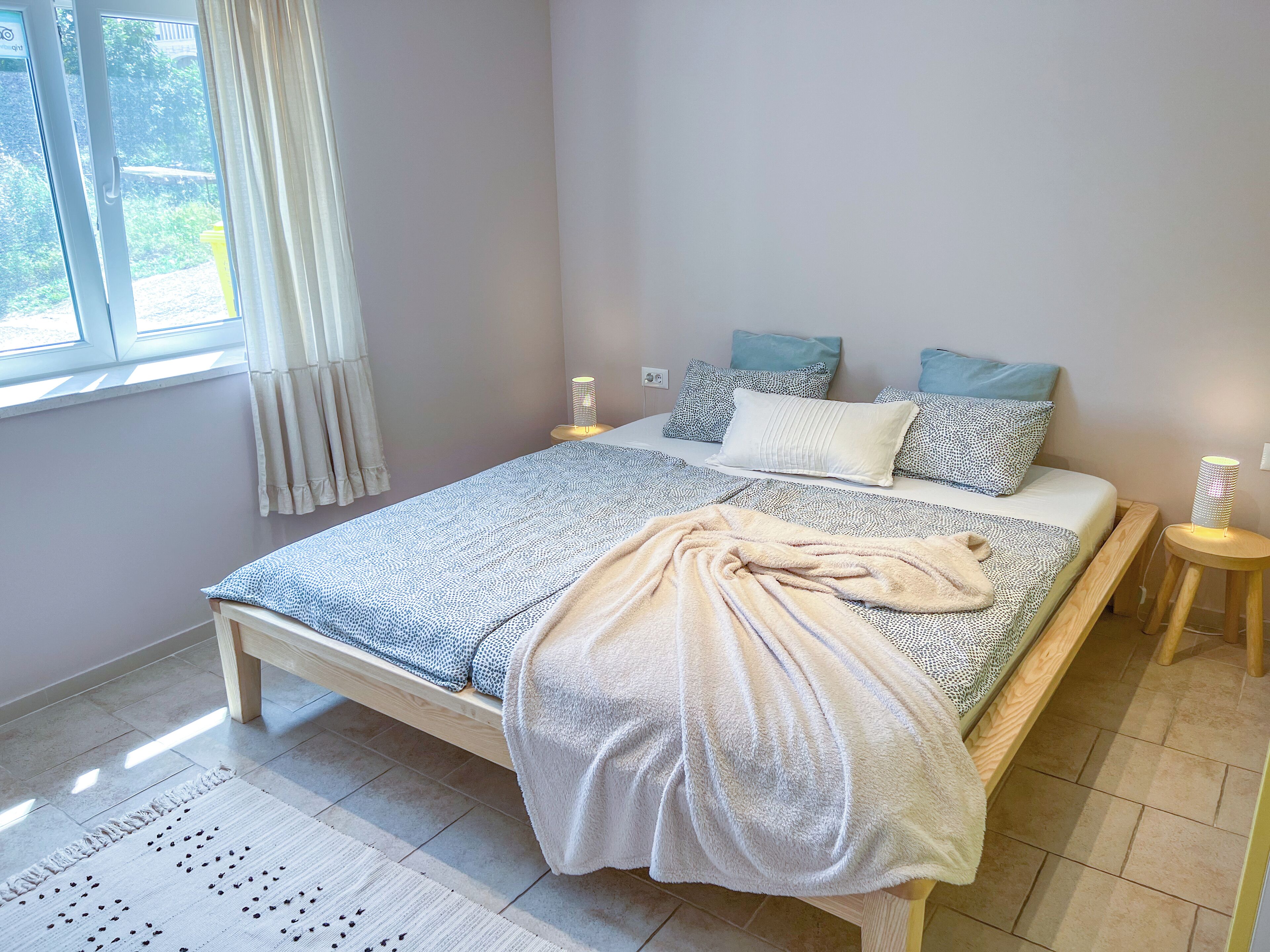 Ein Schlafzimmer mit Bett, Nachttischen, einem Fenster mit Vorhängen und einem Heizkörper.