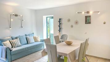 A modern living room with a light blue sofa, a dining table with chairs, and a window with a view of greenery.