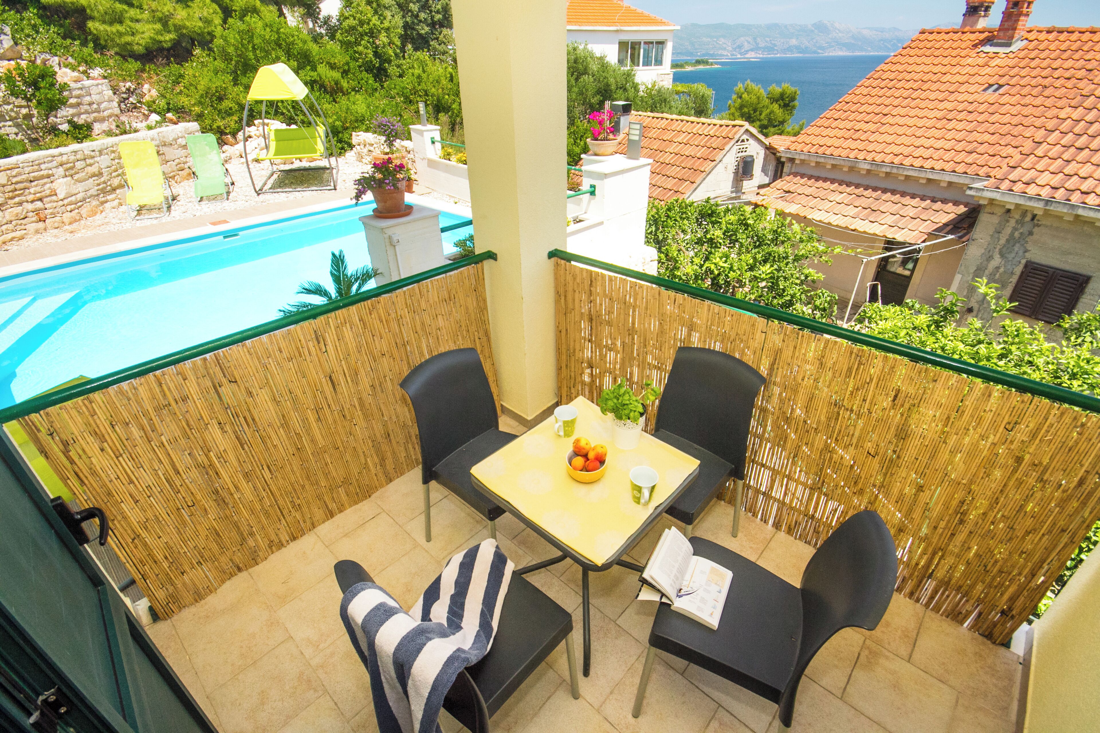A balcony with a pool view, outdoor seating, and a table with a bowl of fruit.