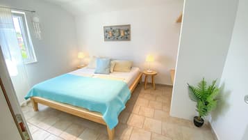 A bedroom with a bed, bedside lamps, a small table, a potted plant, and a wall-mounted artwork.