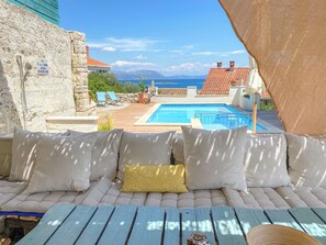 Zona de piscina con asientos acolchados, una piscina y vistas al mar.