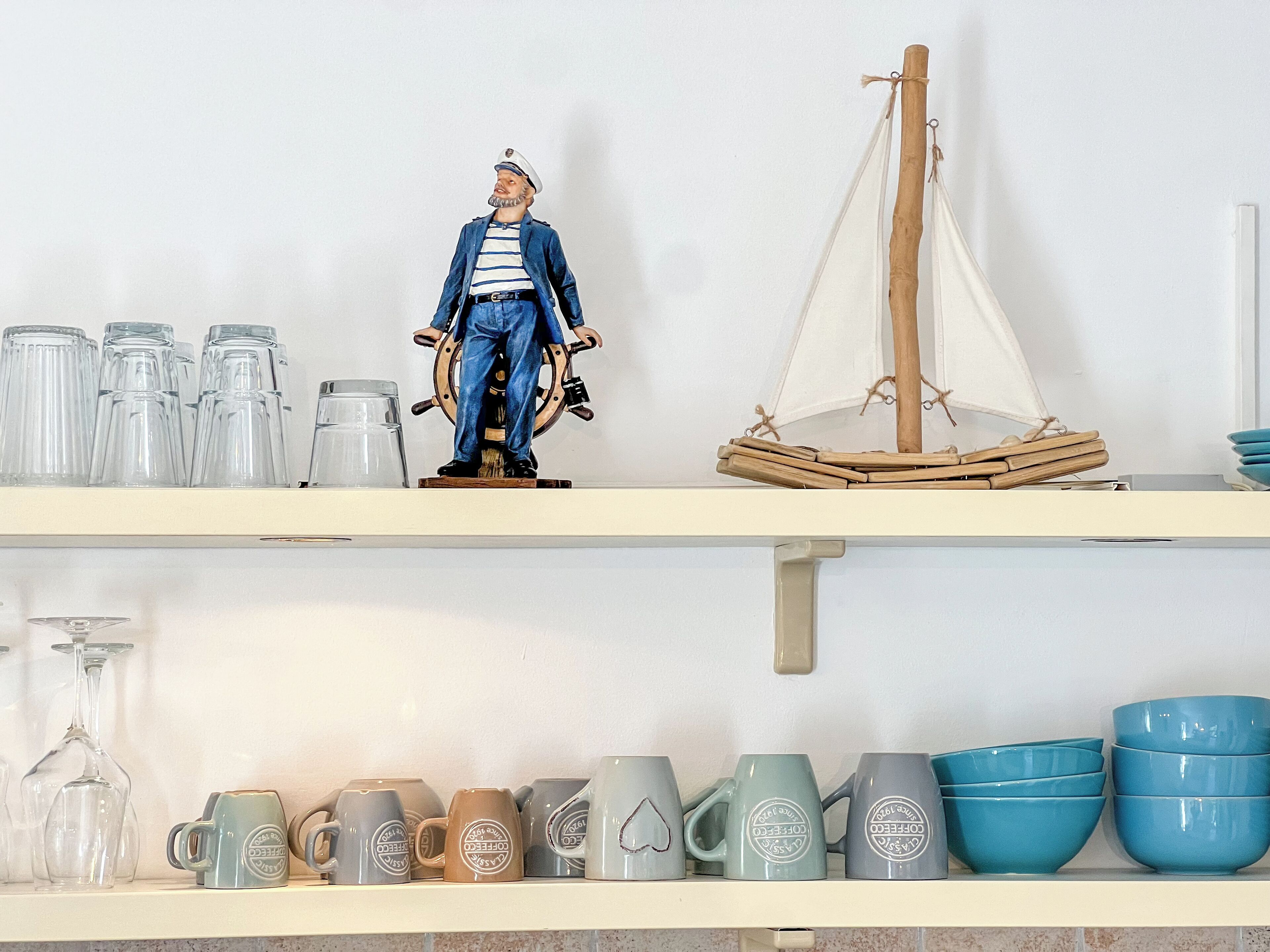 Una estantería con varios objetos, incluyendo una figurita, un modelo de velero y una colección de tazas y cuencos.