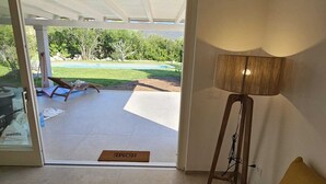 Una habitación con sofá amarillo, una lámpara y vistas a un patio con piscina y vegetación.