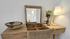 Un escritorio de madera con una silla de fibras naturales, un espejo, una lámpara y una planta en maceta.