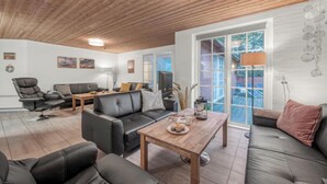 Una sala de estar moderna con techo de madera, sofás de cuero negro, una mesa de centro de madera y un amplio ventanal corredero que da a un área exterior.