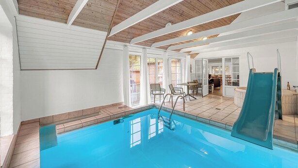Una piscina interior con tobogán, vigas de techo de madera y vistas a un comedor.