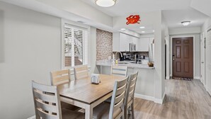 Une cuisine moderne avec des meubles blancs, une table à manger en bois et une décoration représentant un crabe rouge.