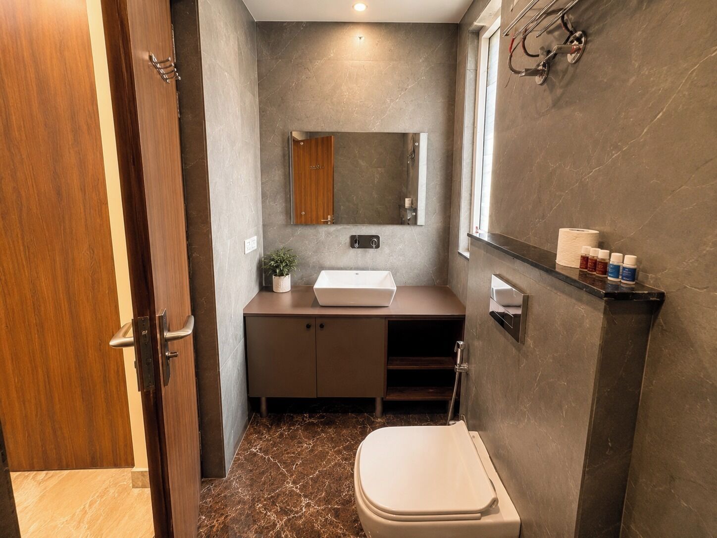A modern bathroom with a marble floor, a white sink, a toilet, and a mirror above the sink.