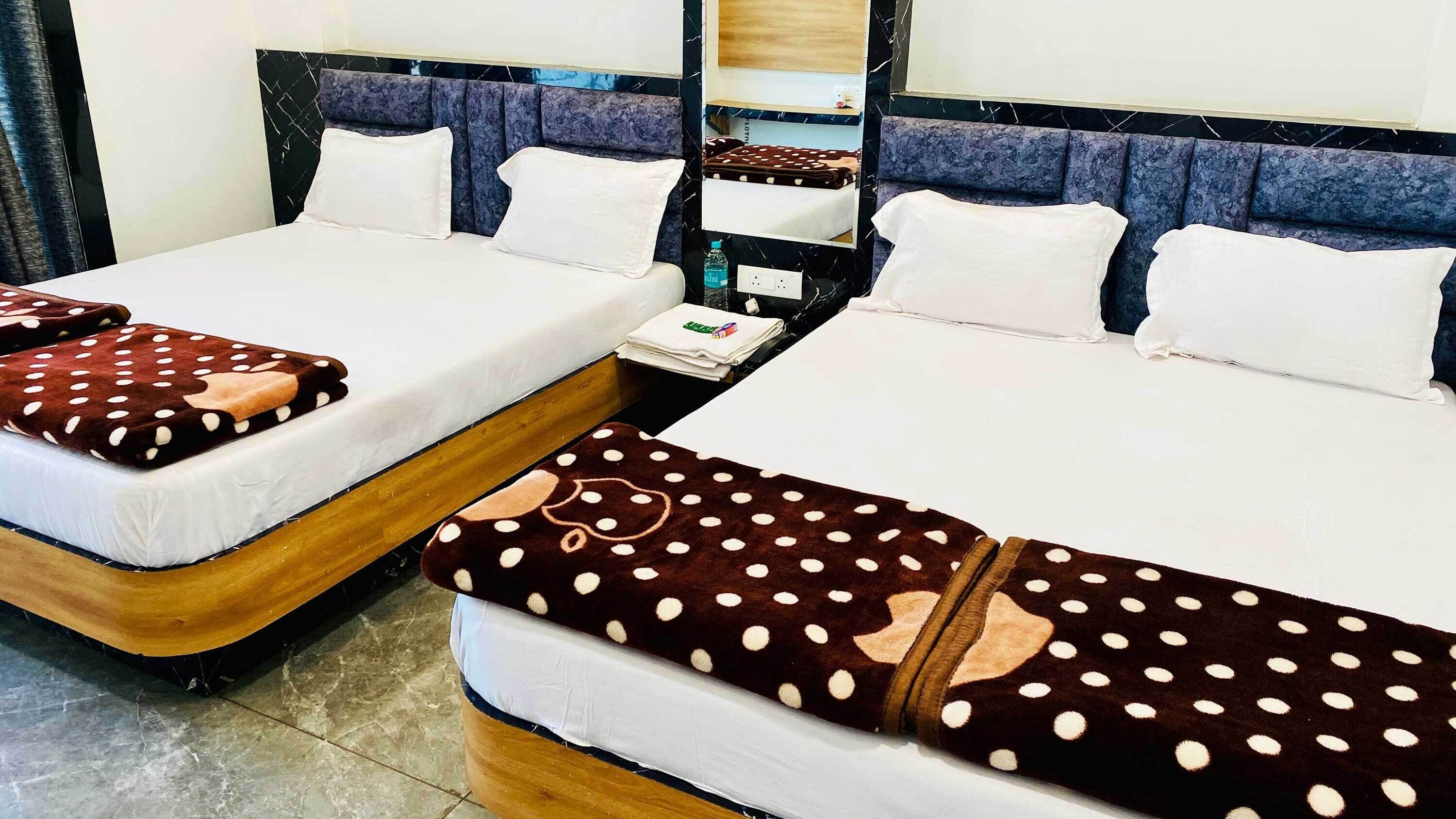 Two double beds with white linens, a marble-patterned headboard, a small bedside table with a bottle and a folded towel, and a mirror above the bed.
