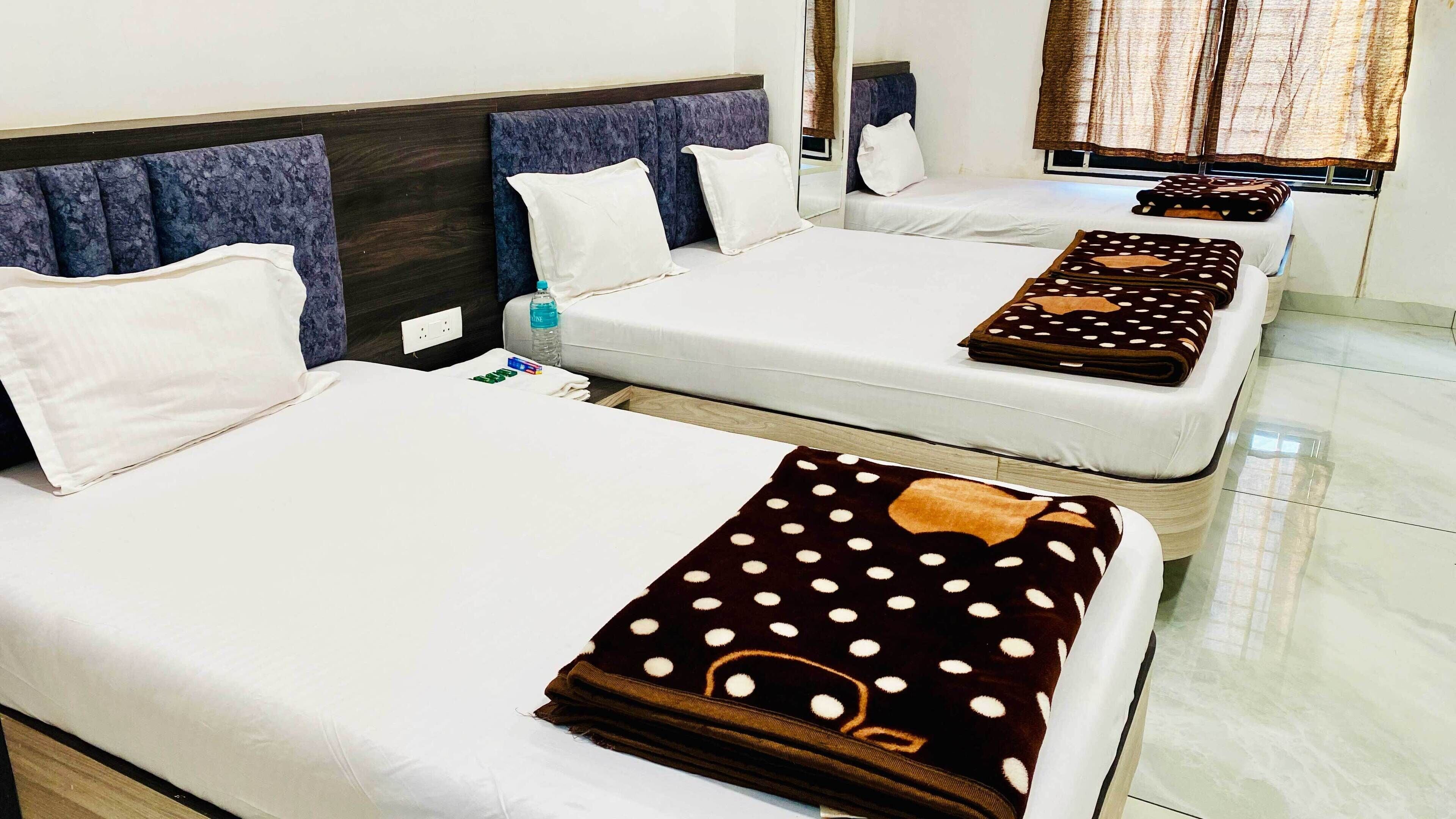 A hotel room with two beds, each with white linens and a dark brown blanket with white polka dots. There is a water bottle on one bed, and a window with curtains.