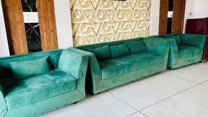 A green sectional sofa in a room with a geometric patterned wall and wooden paneling. - Hotel JK Palace (Khandwa)