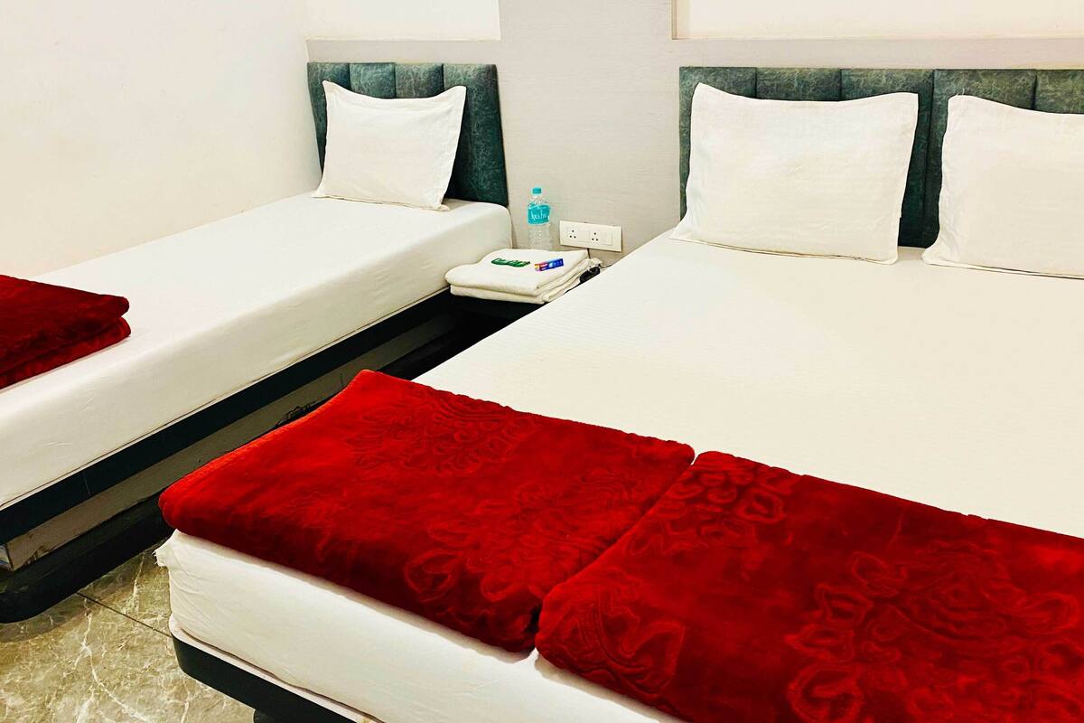 Ein Hotelzimmer mit zwei Betten, jeweils mit weißer Bettwäsche und roten Zierkissen. Auf dem Nachttisch zwischen den Betten steht eine Wasserflasche.
