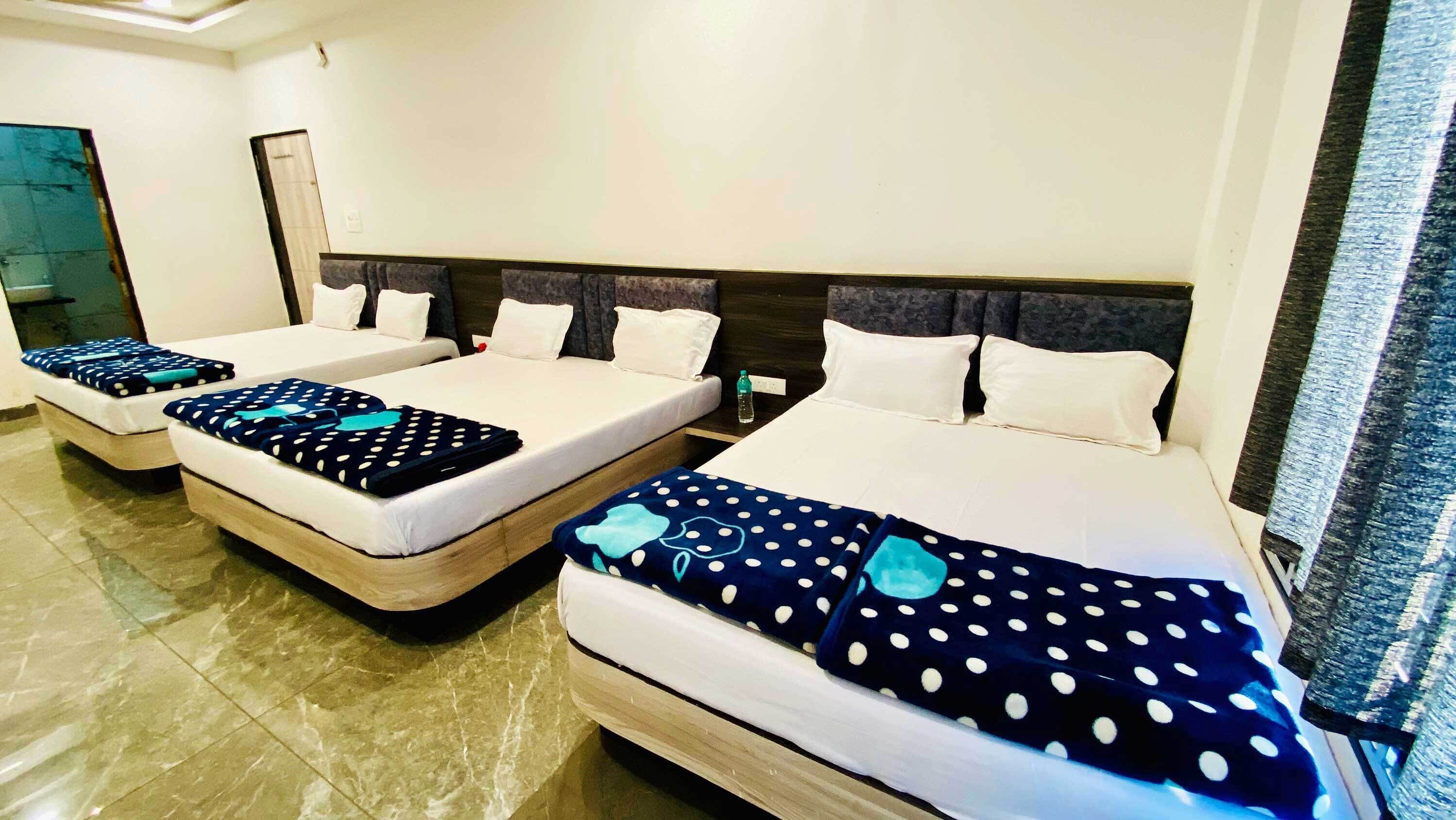 A hotel room with three beds, each with a blue polka dot blanket and white pillows.