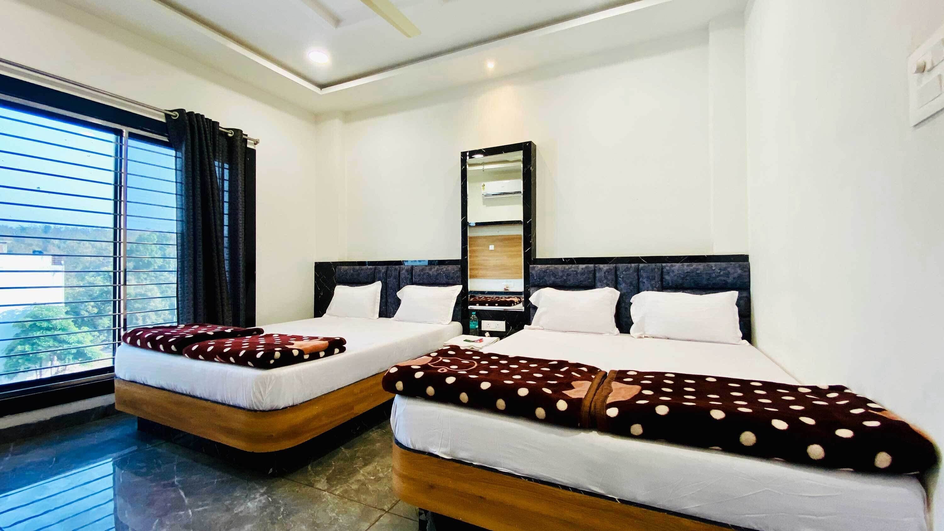 A hotel room with two beds, a large window with blinds, a mirror, and a view of greenery outside.