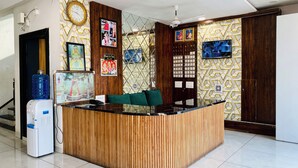 A reception area with a wooden reception desk, a water dispenser, a clock, and framed pictures on the walls. - Hotel JK Palace (Khandwa)