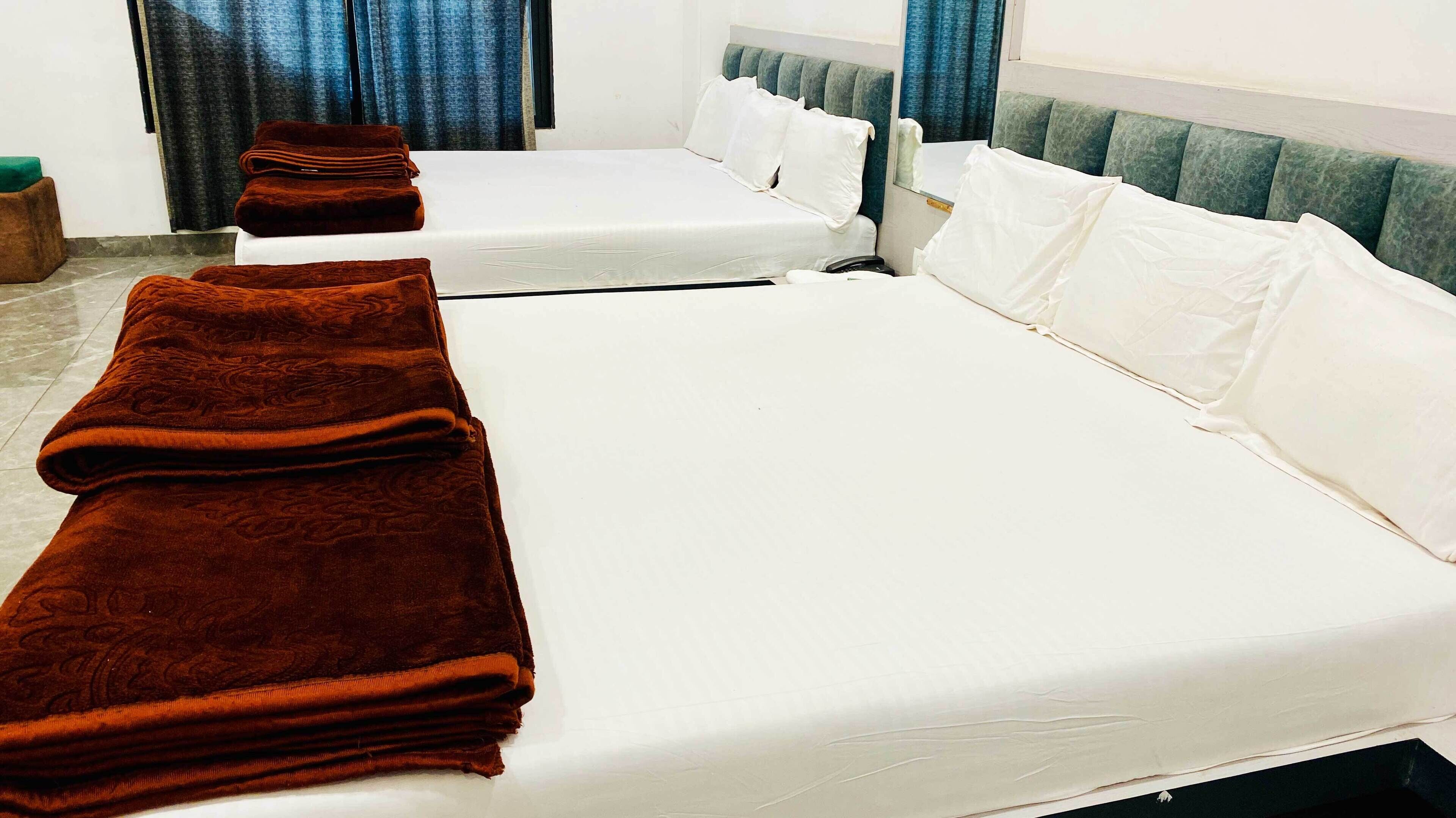 Habitación de hotel con dos camas, cada una con sábanas blancas y mantas marrones.