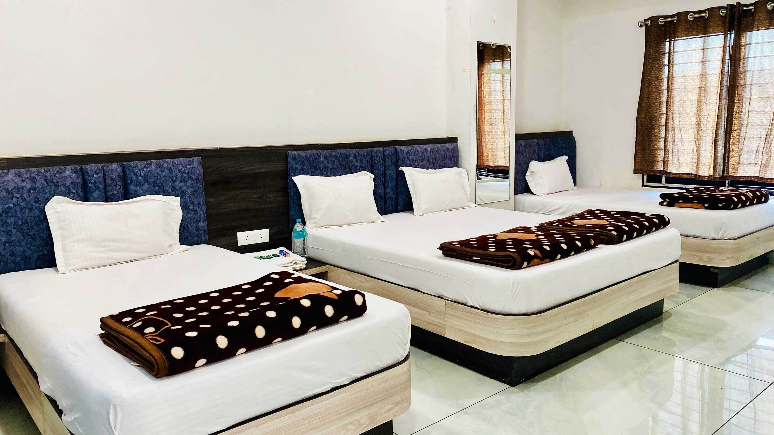 Ett hotellrum med två sängar, båda med vita sängkläder och ett brunt, prickigt överkast. På nattduksbordet står en vattenflaska, och rummet har en modern design med mörkblå sänggavlar.