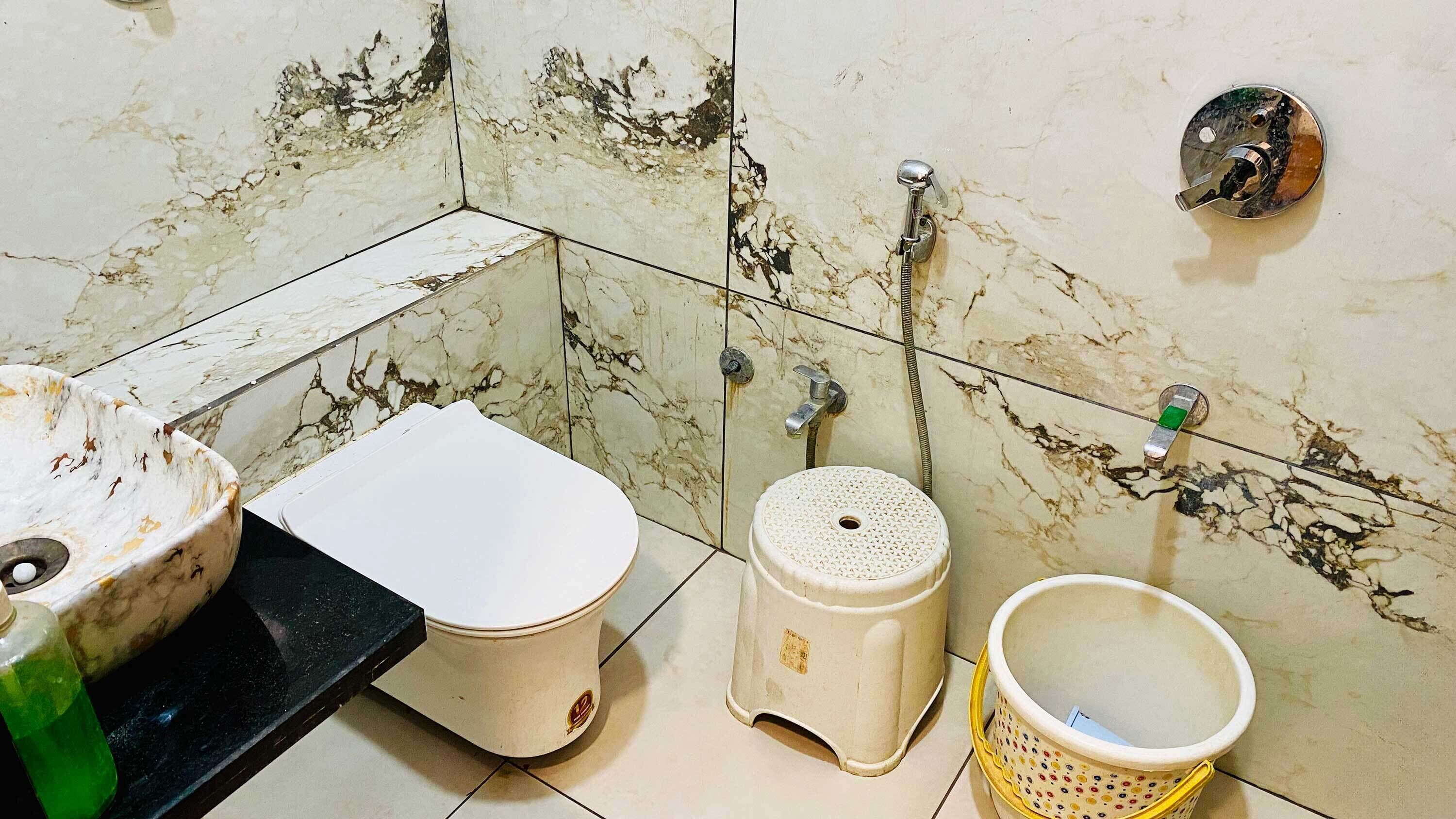 A bathroom with a toilet, bidet, and a small sink with a green bottle.