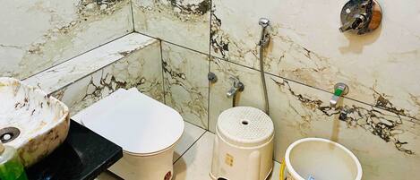 A bathroom with a toilet, bidet, and a small sink with a green bottle.