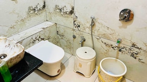 A bathroom with a toilet, bidet, and a small sink with a green bottle. - Hotel JK Palace (Khandwa)