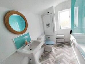 Bathroom features a sink, toilet, and window with a herringbone floor and storage cabinet.