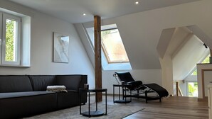 Ein geräumiger Loft mit hoher Decke, einem schwarzen Ledersofa, einem schwarzen Sessel und einem kleinen Tisch.