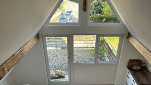 Ein Essbereich mit einem Tisch für vier Personen, eine Küche mit weißen Schränken und Blick auf eine Straße durch große Fenster.
