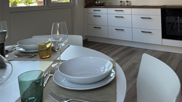 Eine moderne Küche mit weißen Schränken, einem Holzbalken und einem Essbereich mit Tisch für zwei Personen.