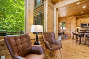 A wooden cabin interior with two leather chairs, a table, a lamp, and a kitchen area with a microwave.