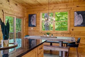 A wooden cabin interior with a dining area, wooden walls, and large windows.