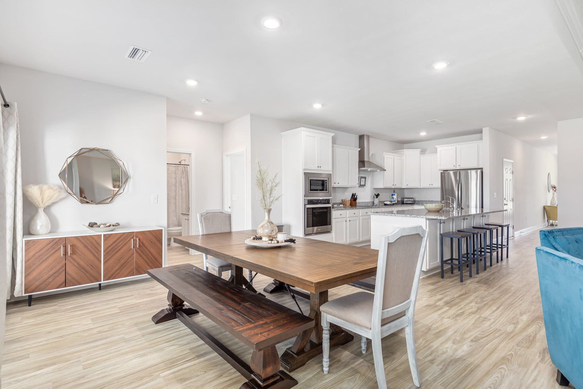 A modern kitchen with white cabinets, stainless steel appliances, and a wooden dining table.