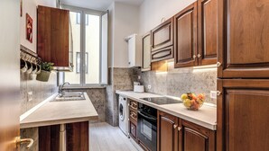 A compact kitchen with wooden cabinets, a built-in oven, a washing machine, and a window providing natural light. - Newly renovated apartment in the heart of Rome. (Roma)
