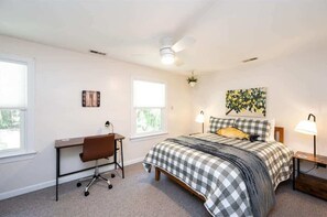 A bedroom with a bed, desk, chair, two windows, ceiling fan, and a wall clock. - Tranquil Retreat w/ Piano, Firepit & Peloton (Pittsboro)