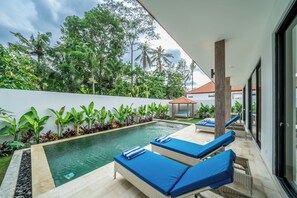 Uma área de piscina moderna ao ar livre, com espreguiçadeiras e um pérgola.